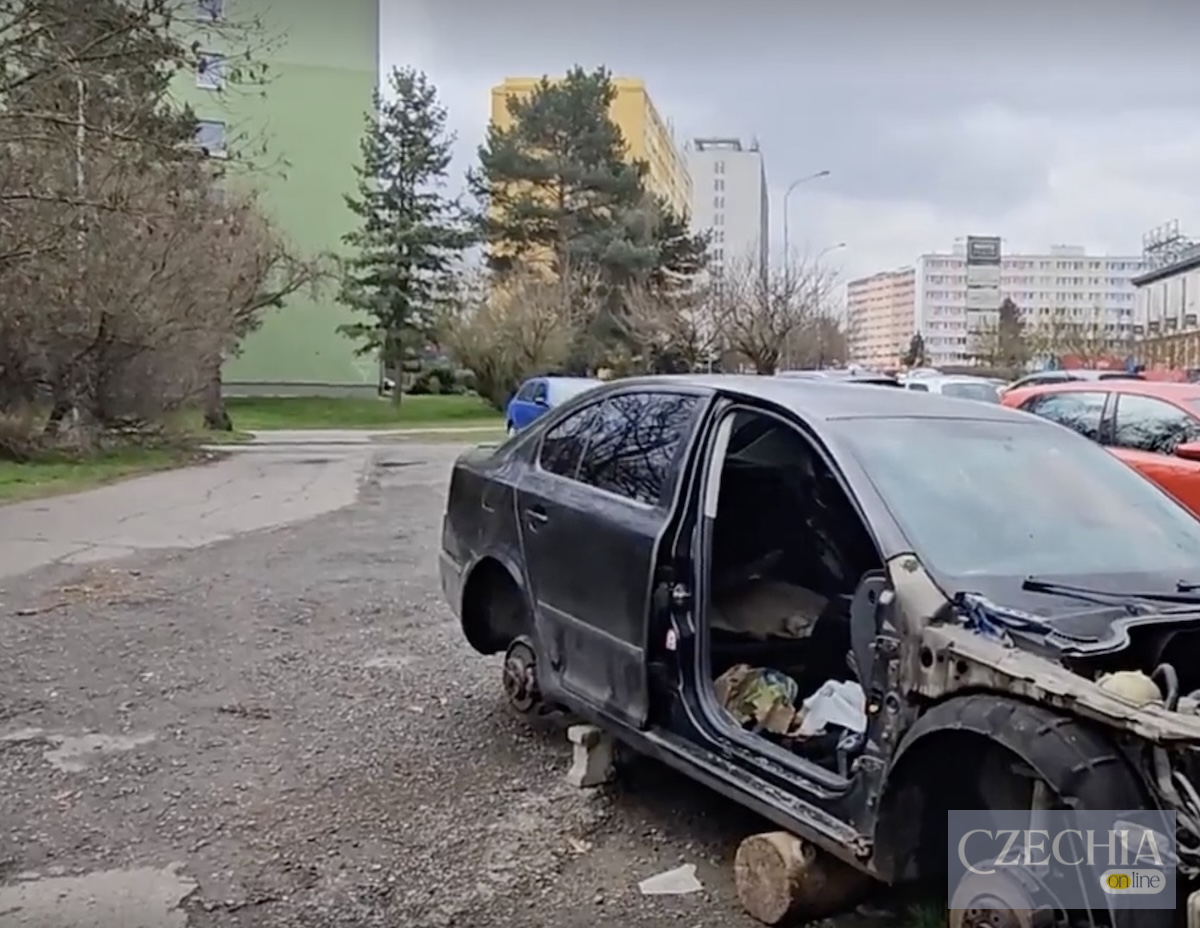 Покинуте авто на парковці Повністю розібране темне авто без коліс і дверей стоїть на колодах біля панельних будинків. Кадри занедбаної території біля лісопарку в Празі.