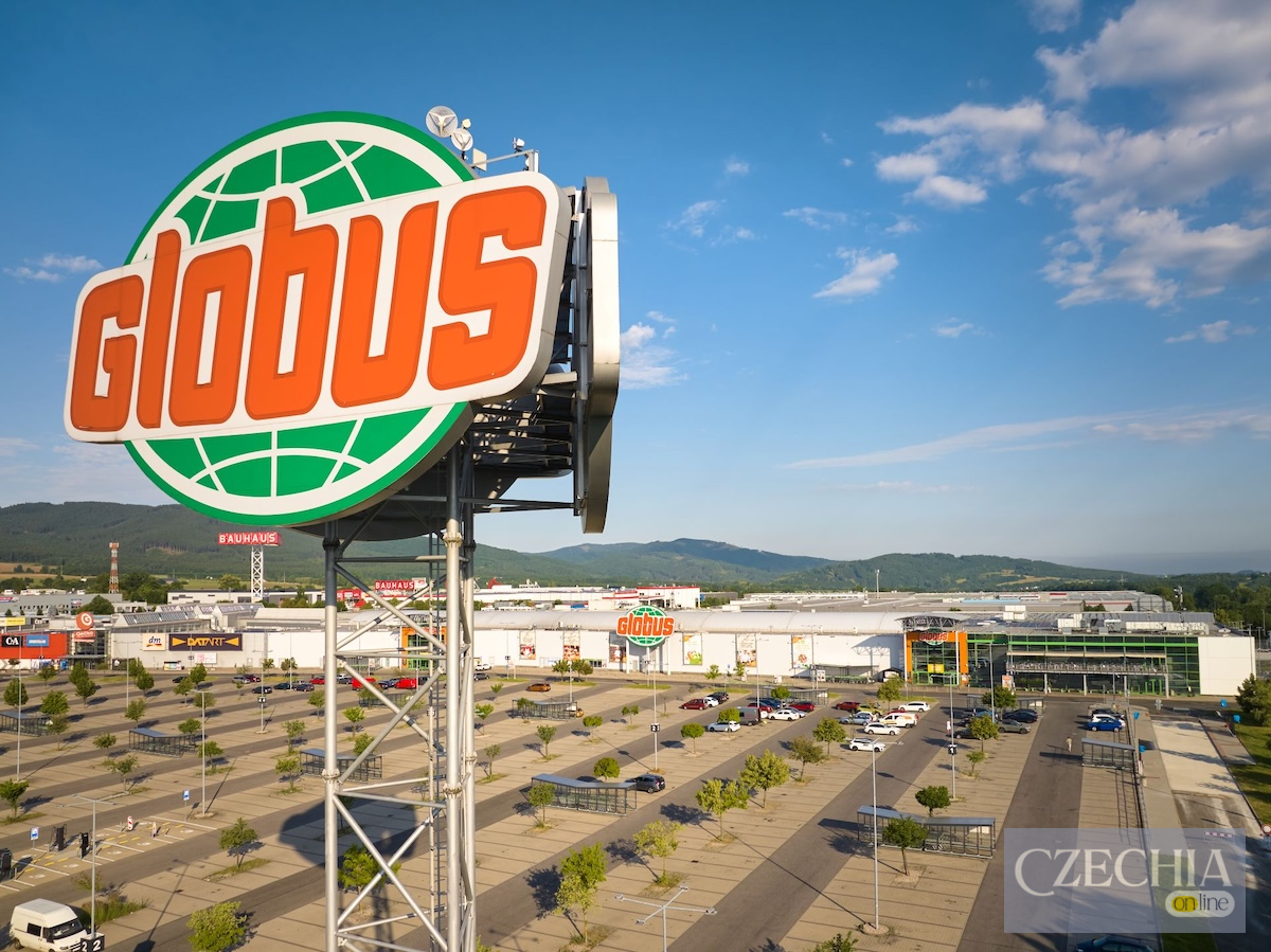 Великий рекламний щит з логотипом супермаркету Globus на тлі просторої парковки та зелених гір. Новина про перевірку якості продуктів у Чехії.