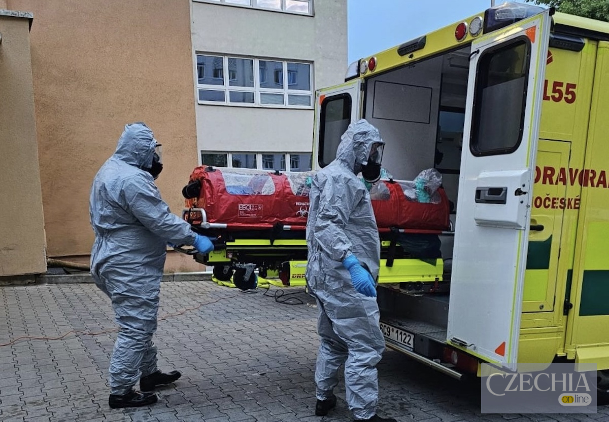 Медики в захисних костюмах завантажують пацієнта в закритому червоному біобоксі до карети швидкої допомоги.