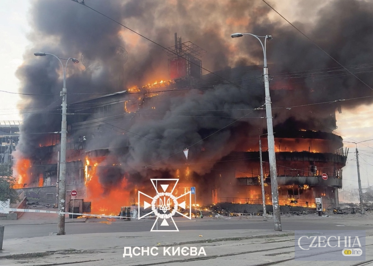 Велика багатоповерхова будівля в Києві охоплена вогнем і густим чорним димом. На передньому плані логотип ДСНС України. Матеріал про обстріл столиці.