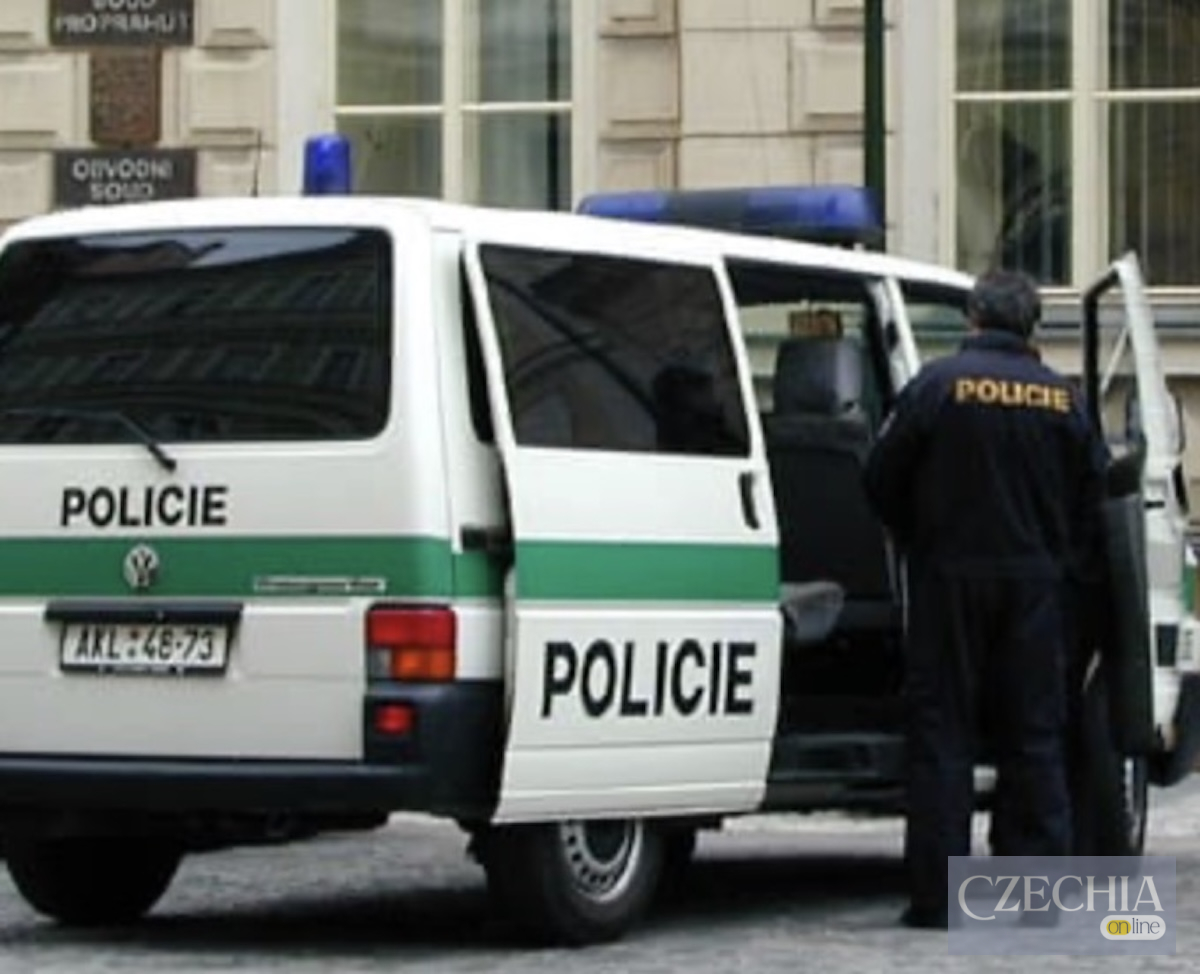 Біло-зелений поліцейський мікроавтобус із відчиненими дверцятами та співробітник поліції у формі на вулиці Праги. Новина про розслідування інциденту з дітьми.