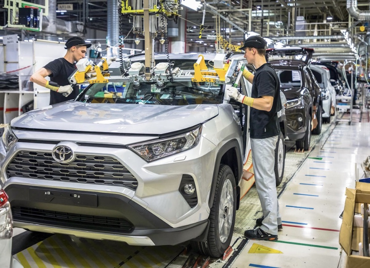 Збирання автомобілів на конвеєрі Toyota Двоє працівників монтують лобове скло на сріблястий автомобіль Toyota RAV4 на сучасному заводському конвеєрі.
