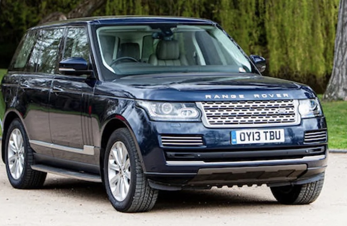 Темно-синій розкішний позашляховик Range Rover припаркований на ґрунтовій доріжці на тлі зелених дерев у парку.