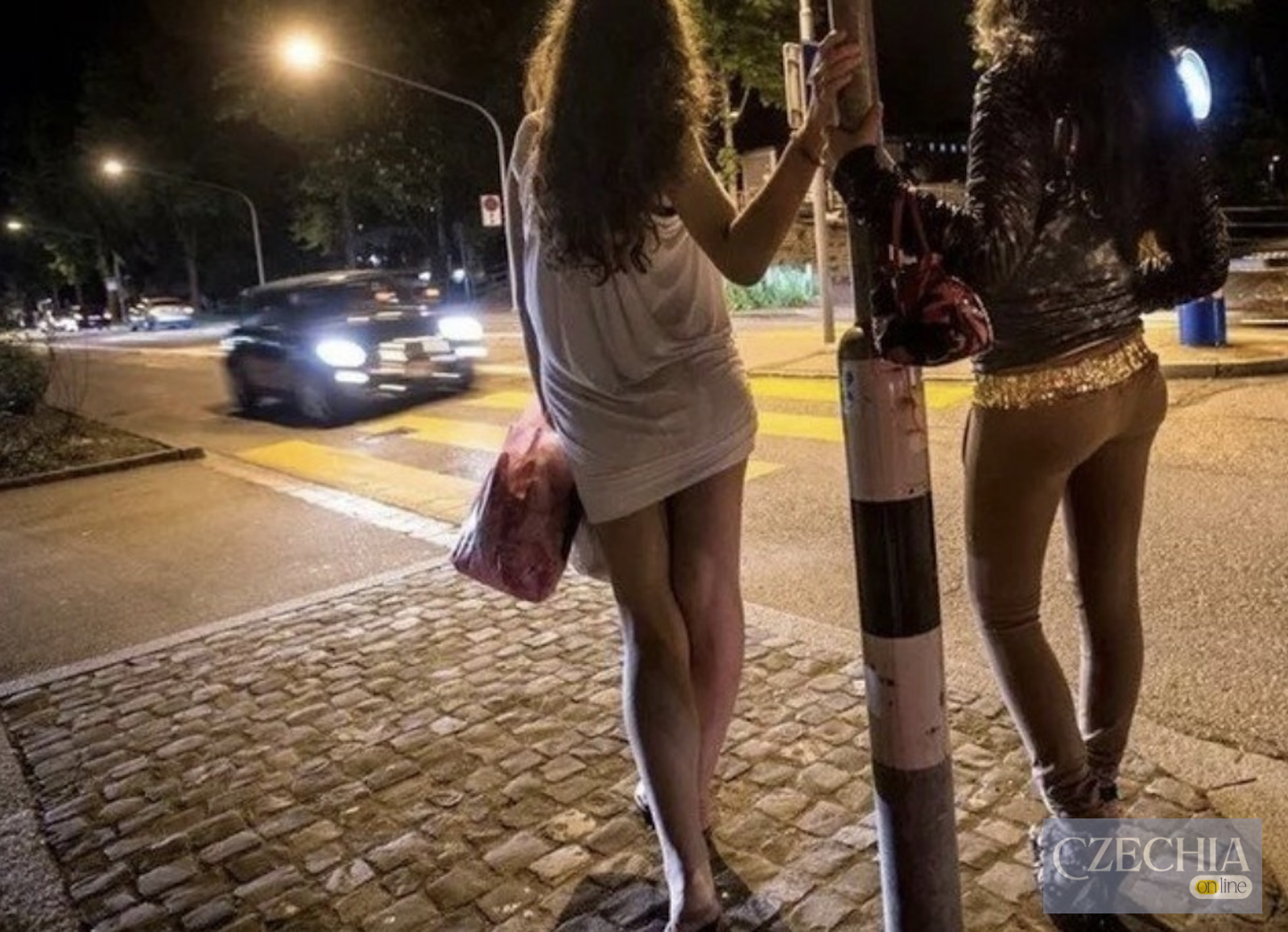 Дві жінки стоять уночі біля дороги на освітленій міській вулиці